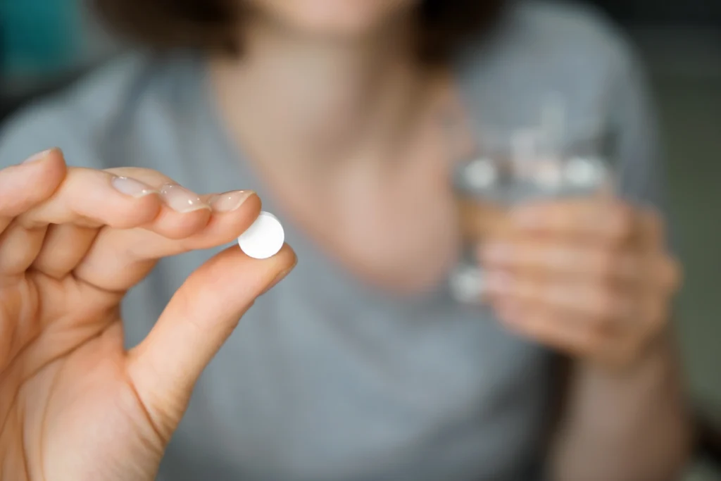 A person holding a pill and a glass of water