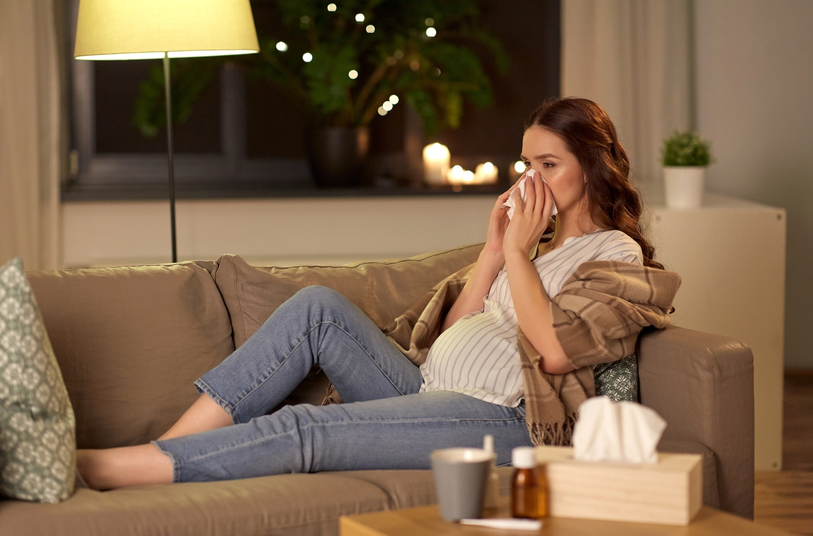 Dextromethorphan During Pregnancy: A pregnant woman on a couch blowing her nose with medication on the table in front of her.