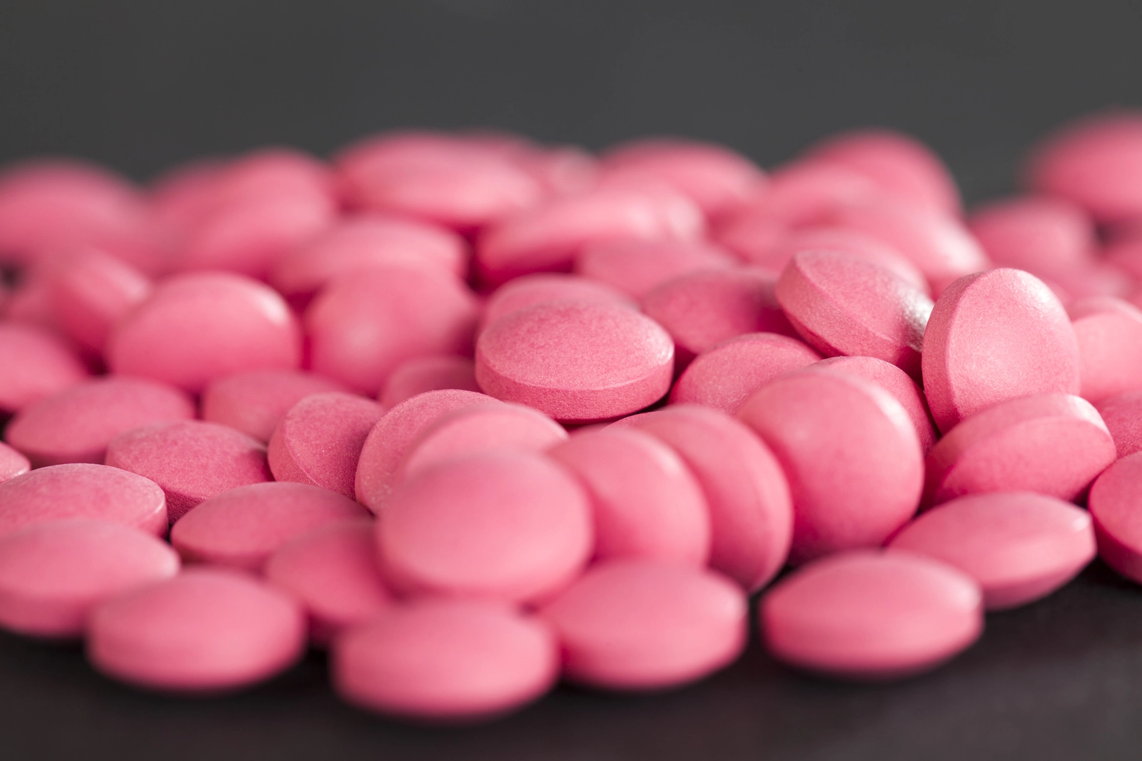 What Is Ibuprofen? A pile of round ibuprofen pills on a dark surface.