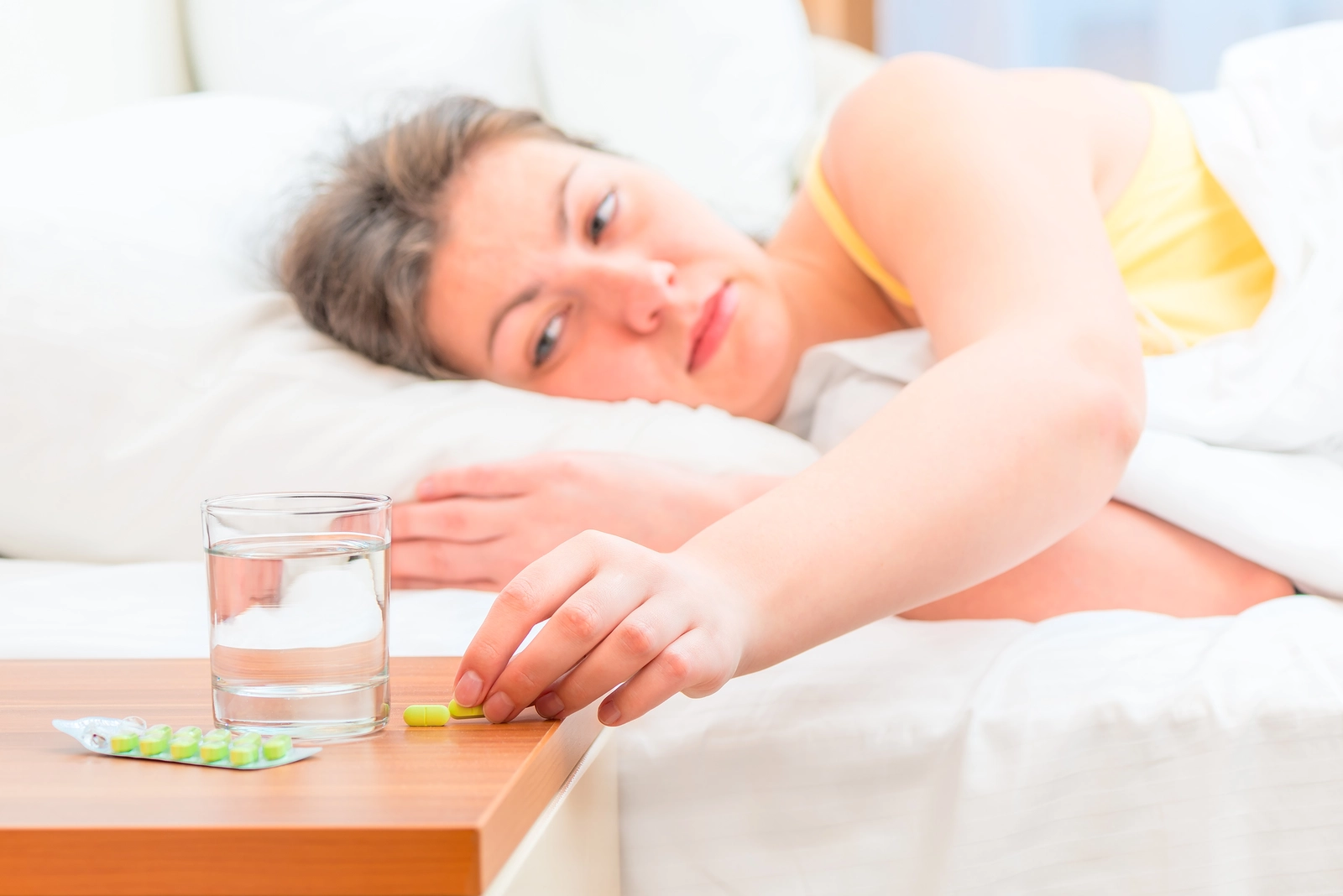 woman laying in bed reaching for medicine