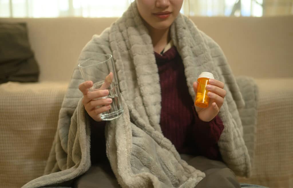 Gabapentin Overdose: A woman sitting wrapped in a blanket with a prescription pill bottle in one hand.